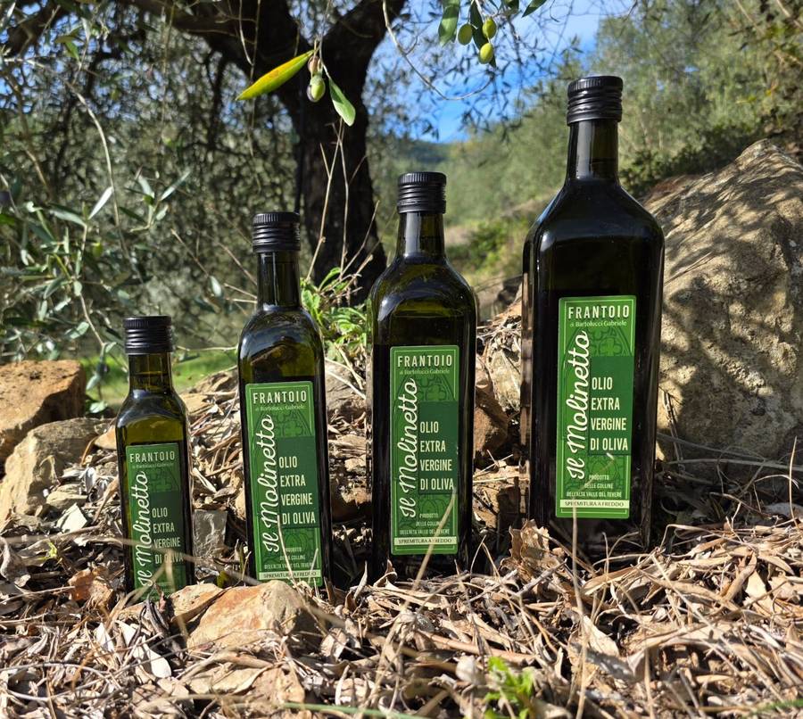Le quattro bottiglie di olio extravergine Il Molinetto, da 250 ml a 1 litro, tra gli ulivi
